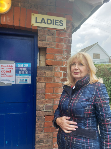 Cllr Jane Lamb pictured next to one of our closed seafront public toilets, as the bustling Fisherman's Green